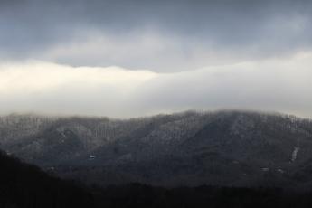 Snow clings to the ground at higher elevations of the mountains as winter storm clouds hang above Tuesday morning. At lower elevations, much of the snow had already melted.