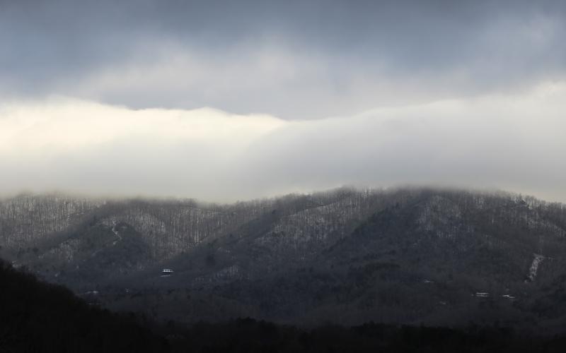 Snow clings to the ground at higher elevations of the mountains as winter storm clouds hang above Tuesday morning. At lower elevations, much of the snow had already melted.