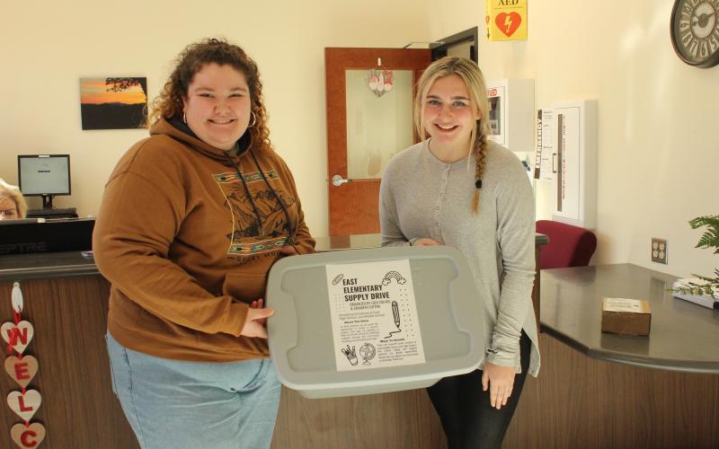 Caption - Swain County High School juniors Sarabeth Sutton (left) and Lola Collins at the high school with the box that will be in the front office to collect donated supplies for East Elementary students.