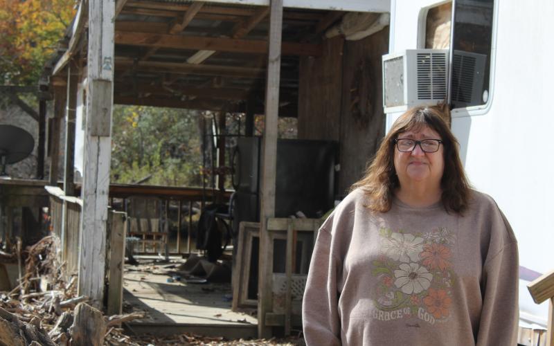 Angela Ellison stands in front of her home and a debris field from Hurricane Helene.