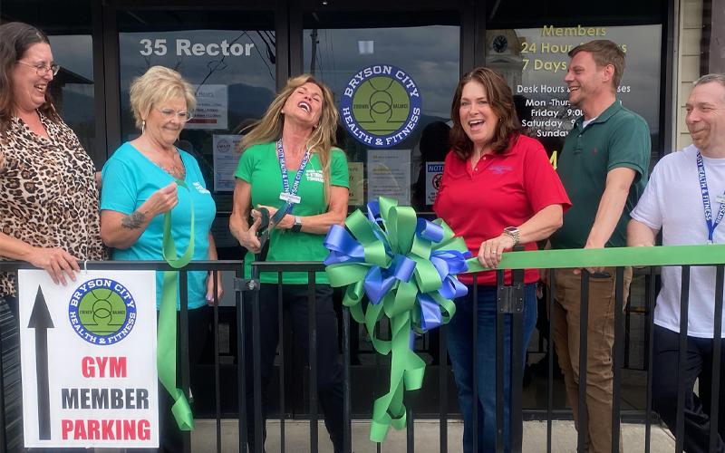 SMT photos/Sara Eisinger.  Michelle Lasky, ambassador at Swain County Chamber of Commerce (left to right), Denene Wolf, gym receptionist, Bibi Pride, gym owner, Monica Brown, chamber president, Ricky Sanford, chamber administrative coordinator, and Anthony Tedesco, personal trainer, gather to cut the yellow ribbon at Bryson City Health and Fitness Saturday, March 29. The chamber currently works with approximately 260 business owners.