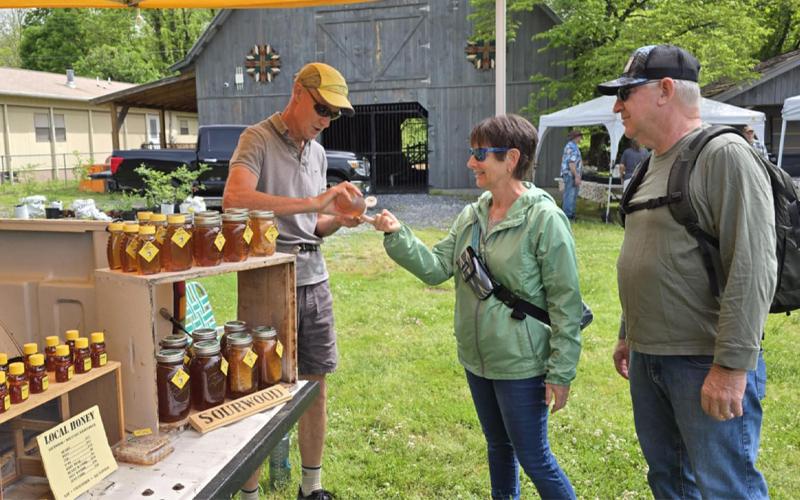 SMT photo/Sara Eisinger. Jim Parham, beekeeper at Smoky Mountain Honey, sells to Mark and Shawn Johnson at the Smoky Mountain Farmers and Artisans Market Friday, May 2. The market will continue through the last Friday in October.