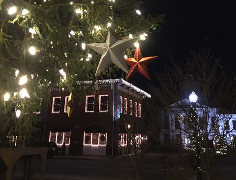 Large star ornaments hang from the town tree. Everett Street Bistro and the Visitors Center are in the background lit up with Christmas lights