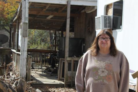 Angela Ellison stands in front of her home and a debris field from Hurricane Helene.