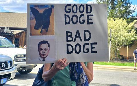 SMT photo/Sara Eisinger.  Demonstrator hides behind ‘GOOD DOGE, BAD DOGE’ sign during a Swain County Democratic Party rally at the corner of Everett and Main Street Saturday, April 5. The party will hold another public rally on International Workers Day, May 1.