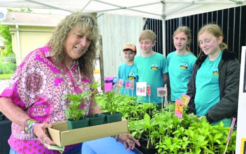 SMT photo/Sara Eisinger.  Barbie Barker buys two marigolds and dwarf cosmos from Sterlin Morefield (left to right), Dainger Rowlan, Charlotte Doughty and Elsa Hayden at the Smoky Mountain Farmers and Artisans Market Friday, May 9. Students have planted and grown more than 1,200 plants in their approximate 8-by-20-foot garden and two small, raised beds this school year.
