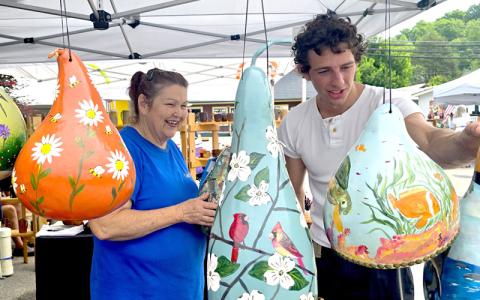 SMT photo/Sara Eisinger.  Susie Q Gourds artist Susan Davis shows gourd art to interested buyer Mitchell Russoti at Railfest in Bryson City Saturday, May 17. Davis will return to sell colorful gourds of all shapes and sizes during Freedom Festival.