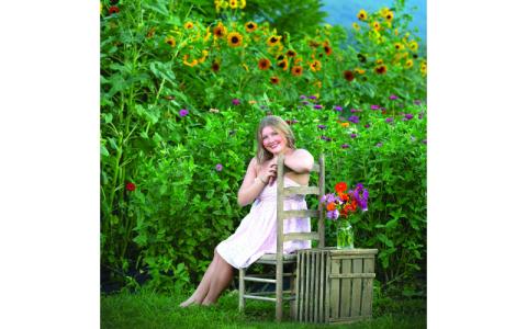 Photo/Michelle Cochran.  A Faith-ful Petals backdrop of colorful wildflowers is picturesque for gardener Brylee Shuler, who basks under the July sun in Deep Creek. Shuler grew the garden in memory of her late father and baby sister.