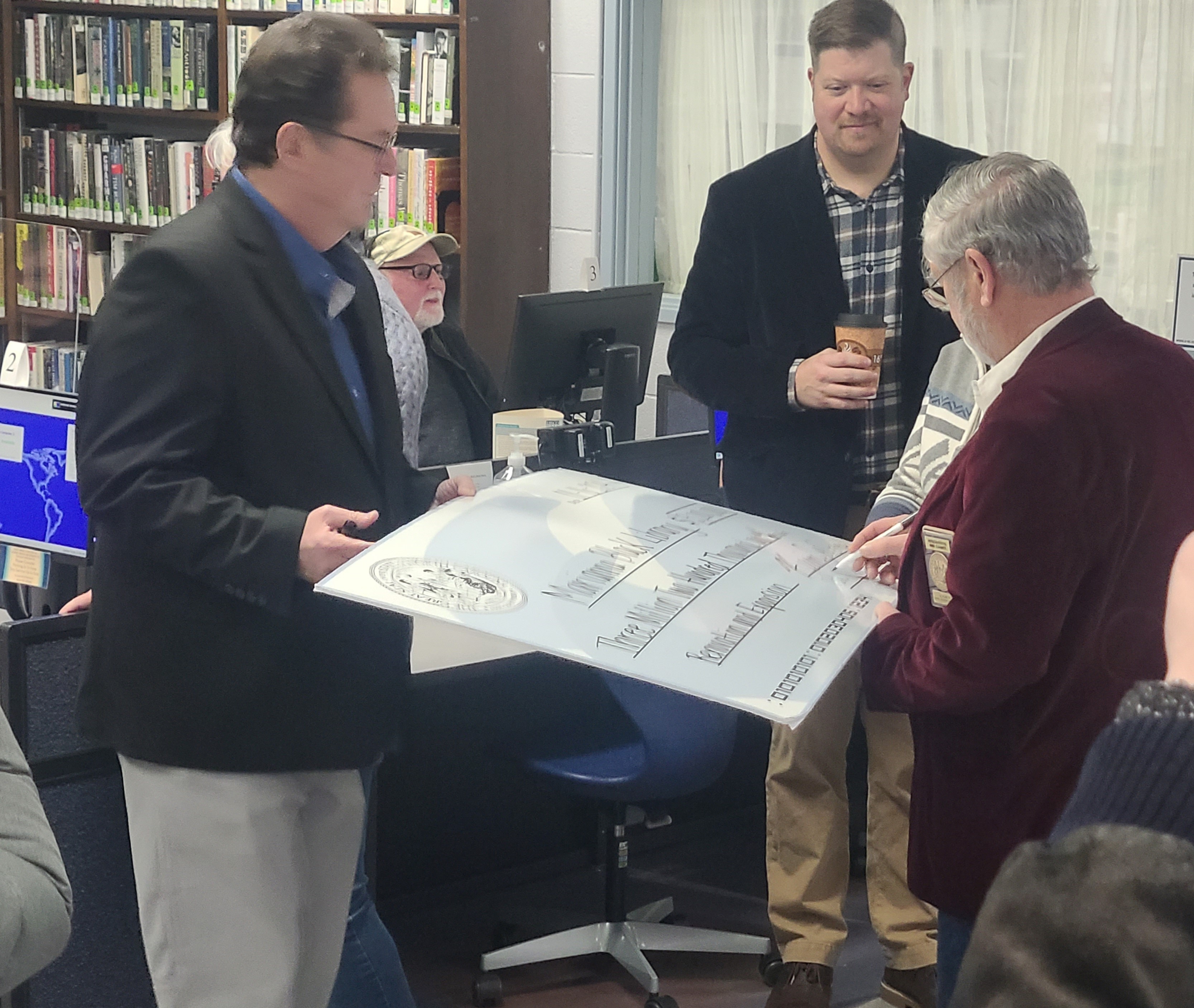 Above, Marianna Black Library Board Member Christian Siewers looks on as N.C. Senator Kevin Corbin (left) and NC Representative Mike Clampitt sign the $3.2 million dollar check for the library expansion and renovation project