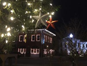 Large star ornaments hang from the town tree. Everett Street Bistro and the Visitors Center are in the background lit up with Christmas lights