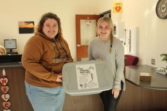 Caption - Swain County High School juniors Sarabeth Sutton (left) and Lola Collins at the high school with the box that will be in the front office to collect donated supplies for East Elementary students.