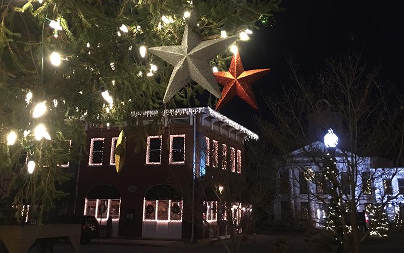 Large star ornaments hang from the town tree. Everett Street Bistro and the Visitors Center are in the background lit up with Christmas lights